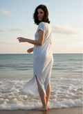 Woman in a flowy blue patterned maxi dress standing at the ocean's edge