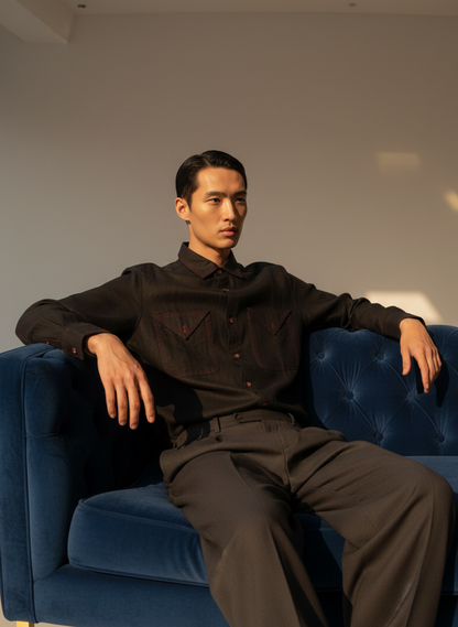 Man in a black outfit sitting on a blue couch against a neutral wall.
