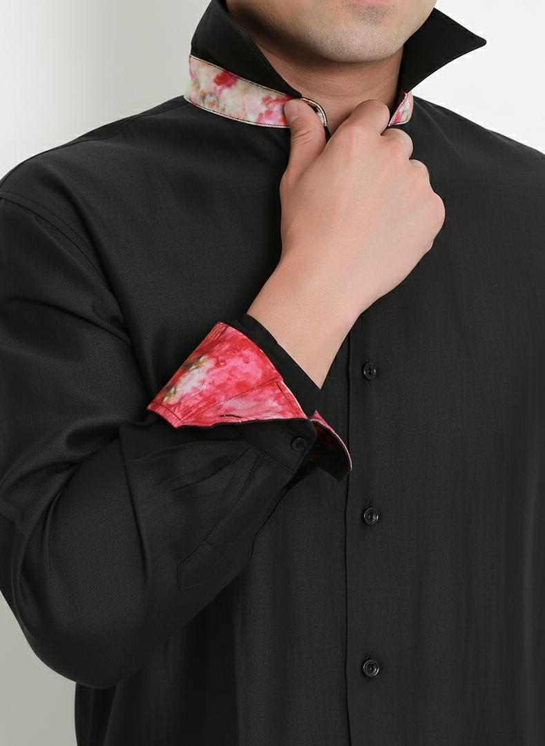 Person wearing a black shirt with floral cuffs and collar against a plain background